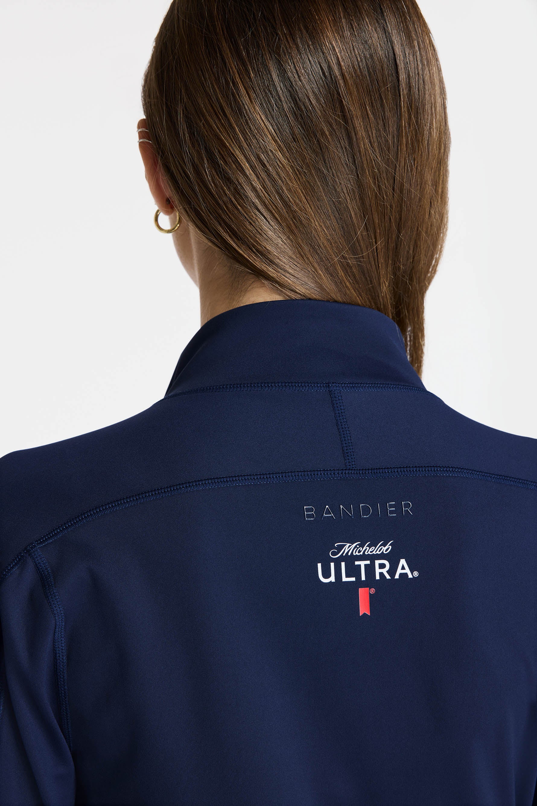 Back view of a model wearing Bandier x Michelob ULTRA Full Zip Jacket, zoomed in on top half, Bandier and Michelob ULTRA branding on top center back