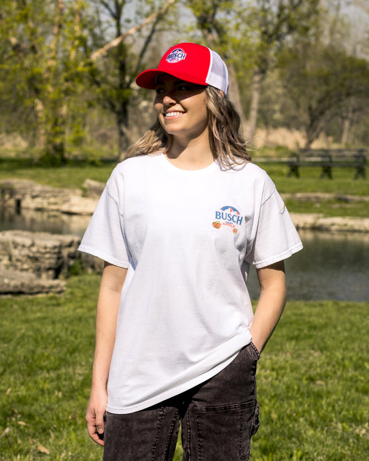 Person wearing a red and white cap and white t-shirt with a logo, standing outdoors.