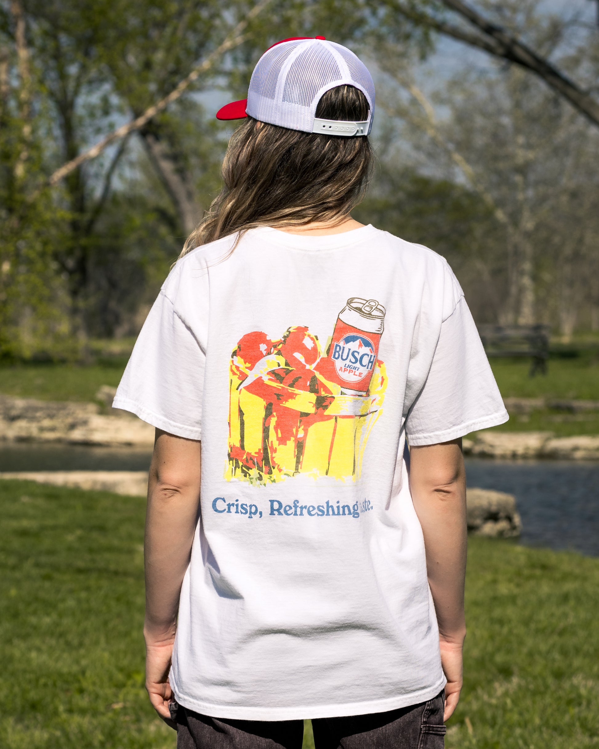Person wearing a white t-shirt with a colorful graphic and 'Busch' branding, standing outdoors.