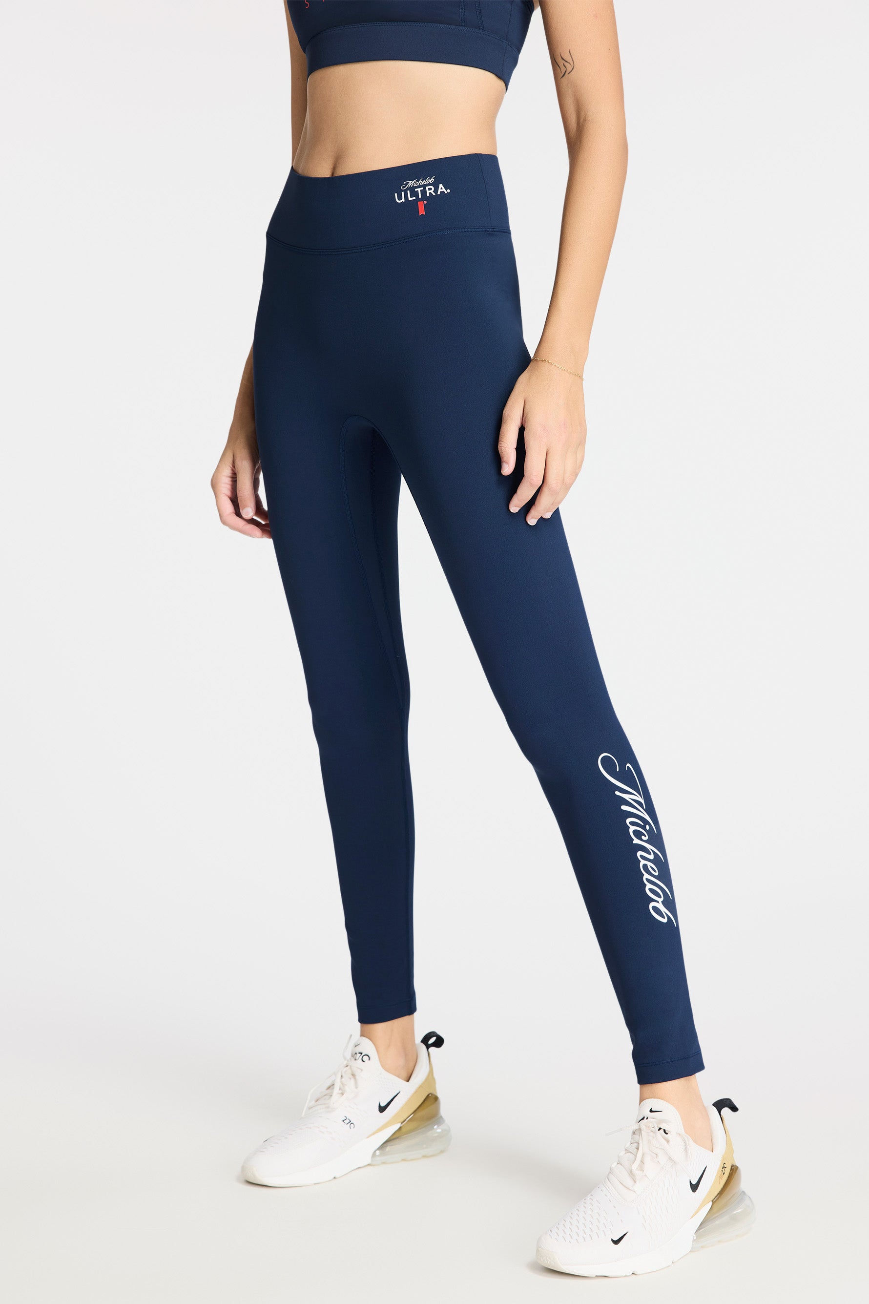 Bottom half of model wearing Bandier x Michelob ULTRA Center Stage Leggings, Michelob Ultra logo on left waistband, "Michelob" on left pants leg