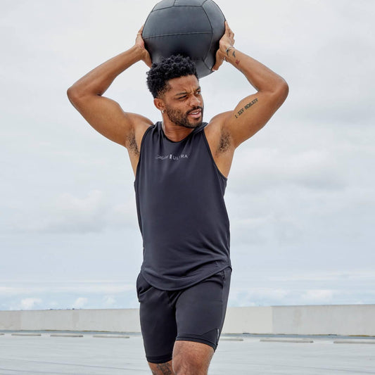 man holding ball weight in short and tank