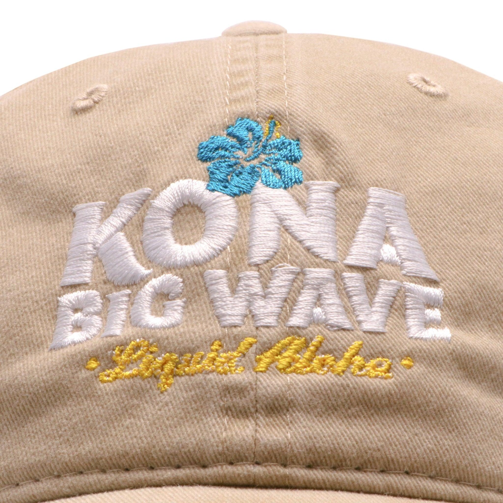 close up of front hat logo. Embroidered Kona Big wave in white with Liquid aloha in yellow below with blue hibiscus flower