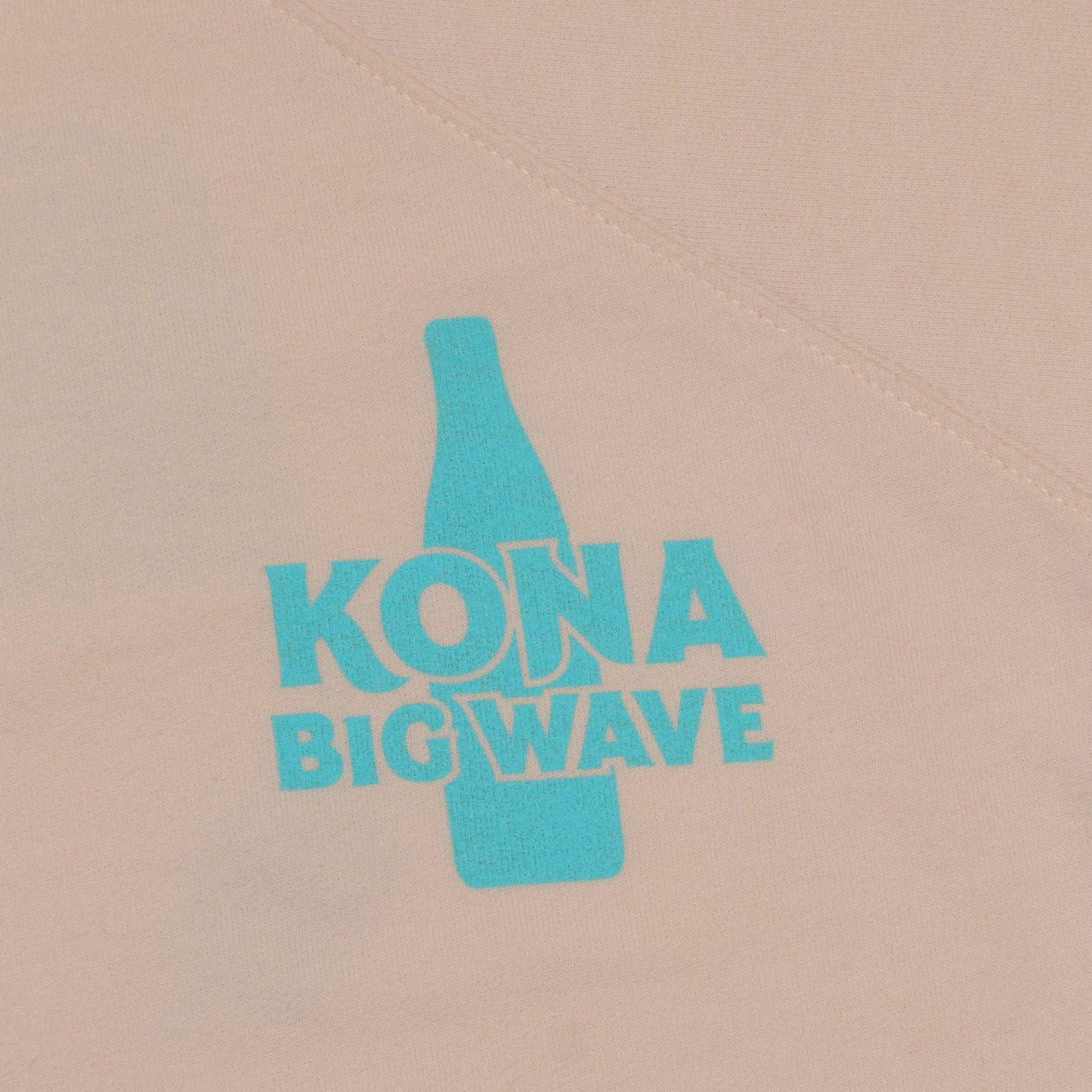 close up of front left chest logo with Kona Big Wave with bottle behind