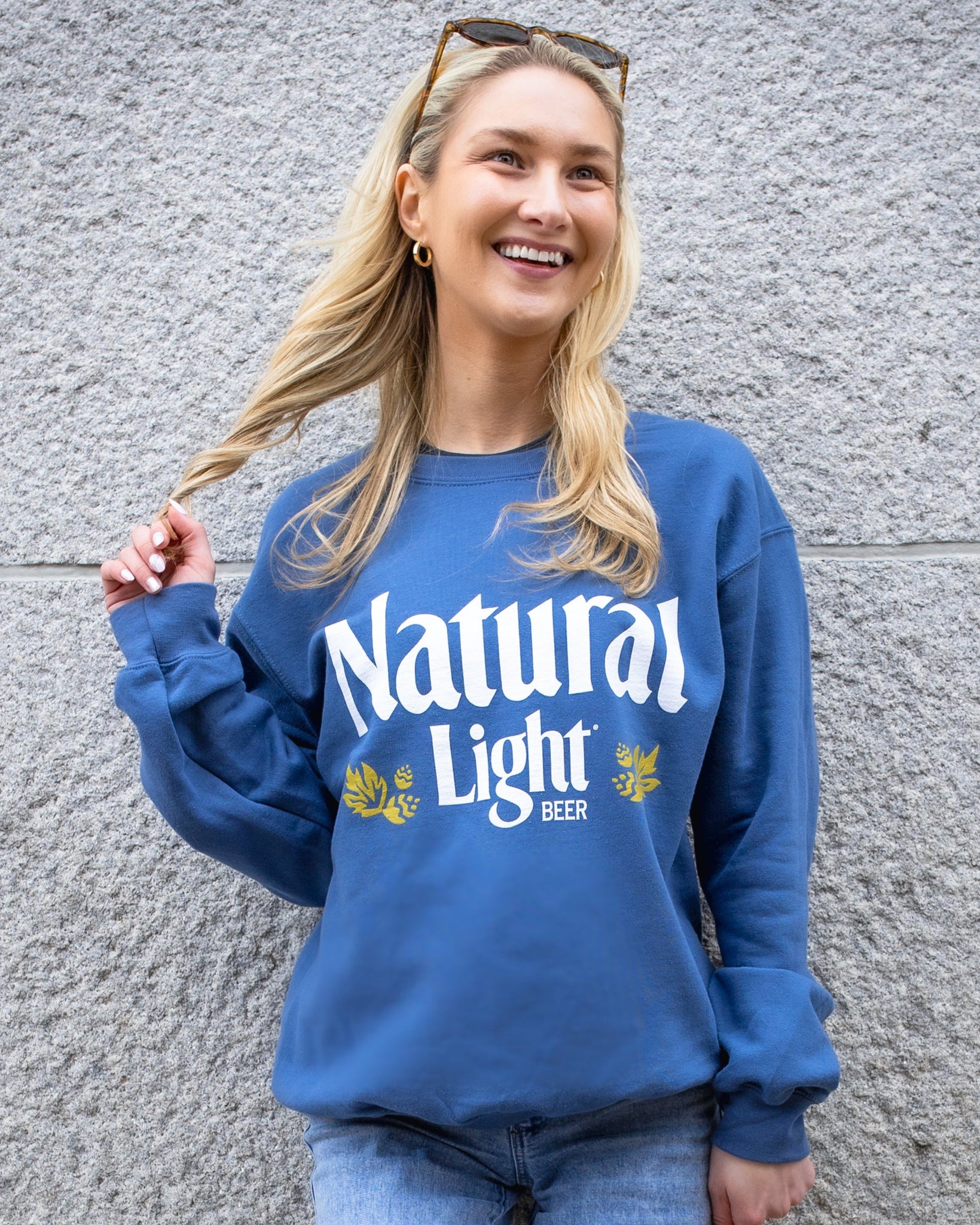 Person wearing a blue 'Natural Light' sweatshirt against a gray wall
