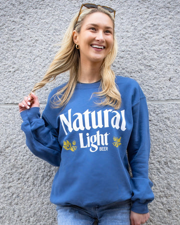 Person wearing a blue 'Natural Light' sweatshirt against a gray wall