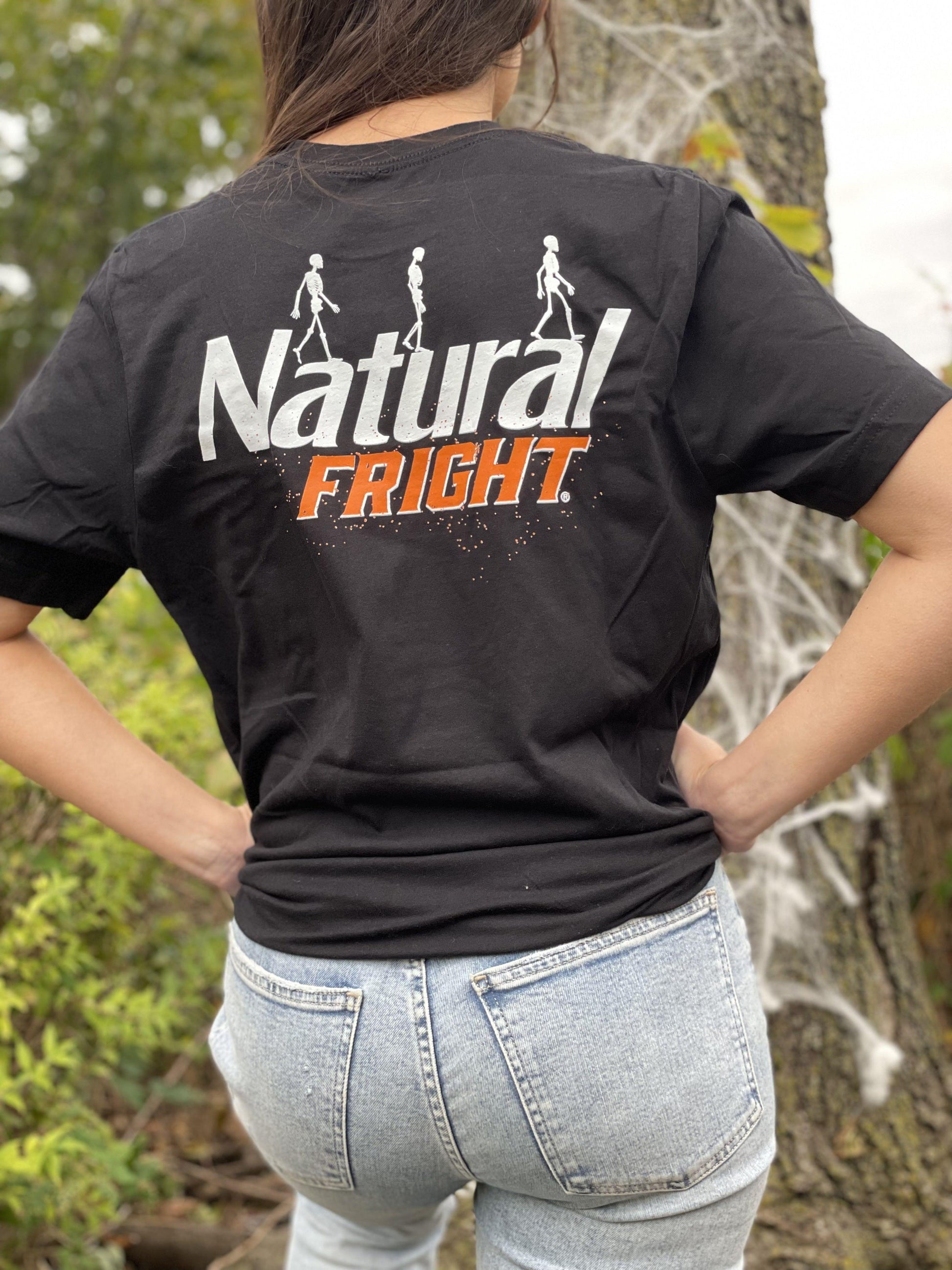 woman wearing black natural light backprint t shirt with natural light logo in white and orange on the back of shirt with white skeletons walking across logo