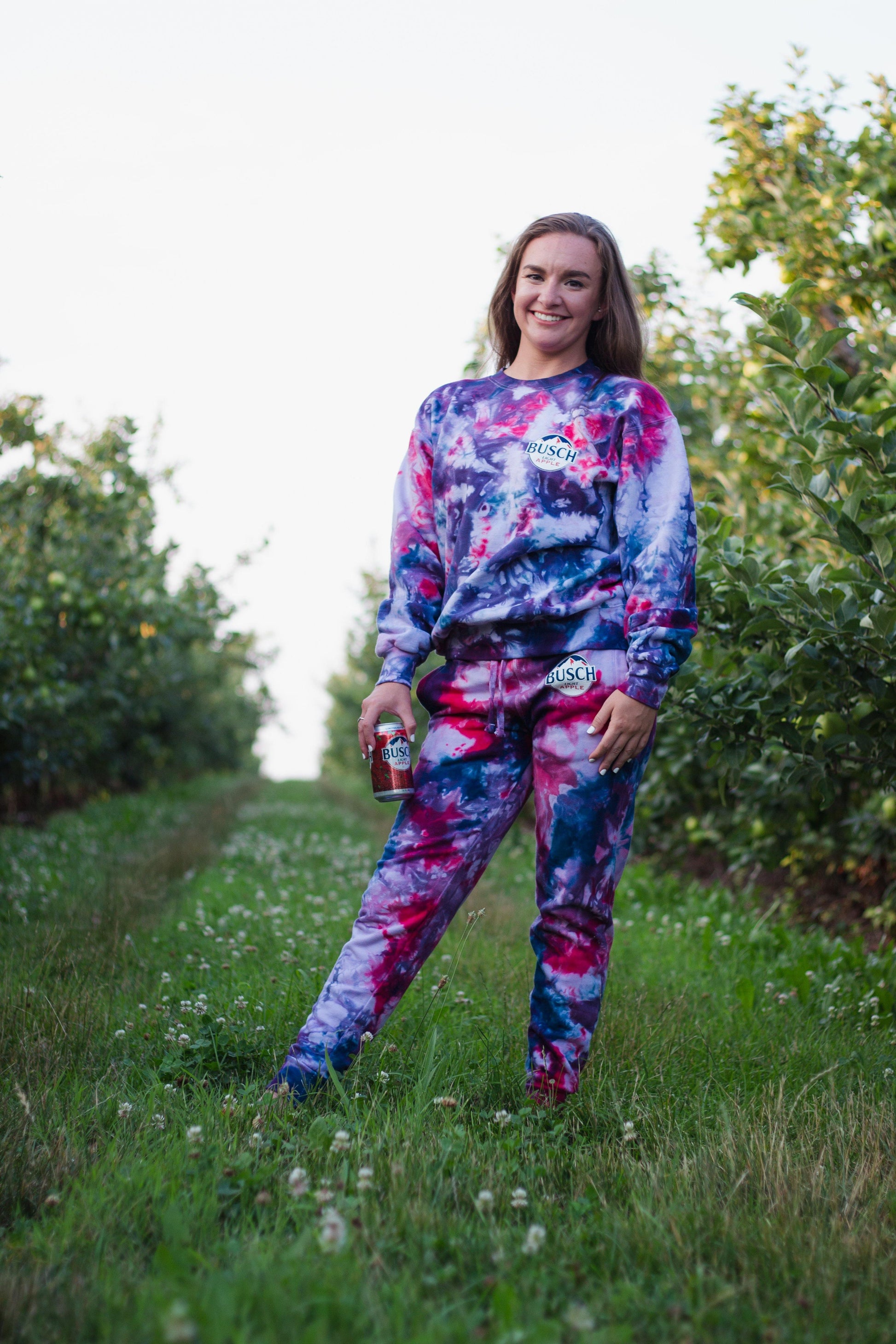 woman wearing busch light apple tie dye joggers outside while holding busch light apple can